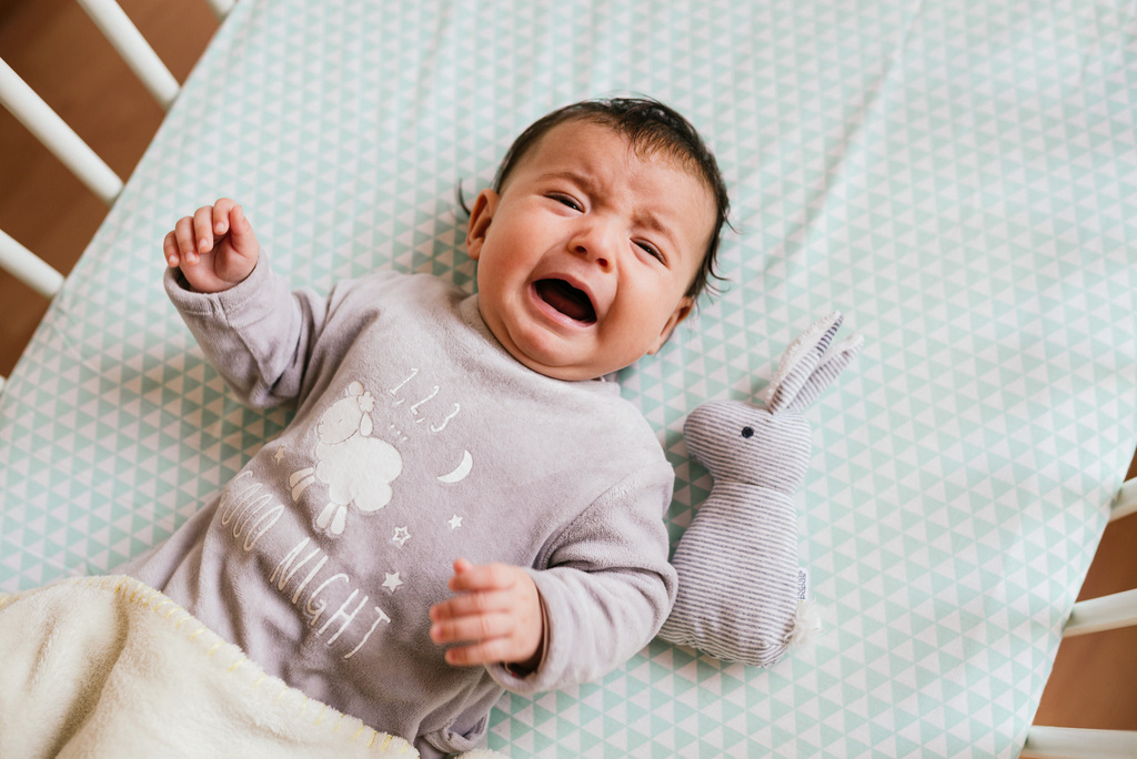 Humana Baby liegt im Bett und weint